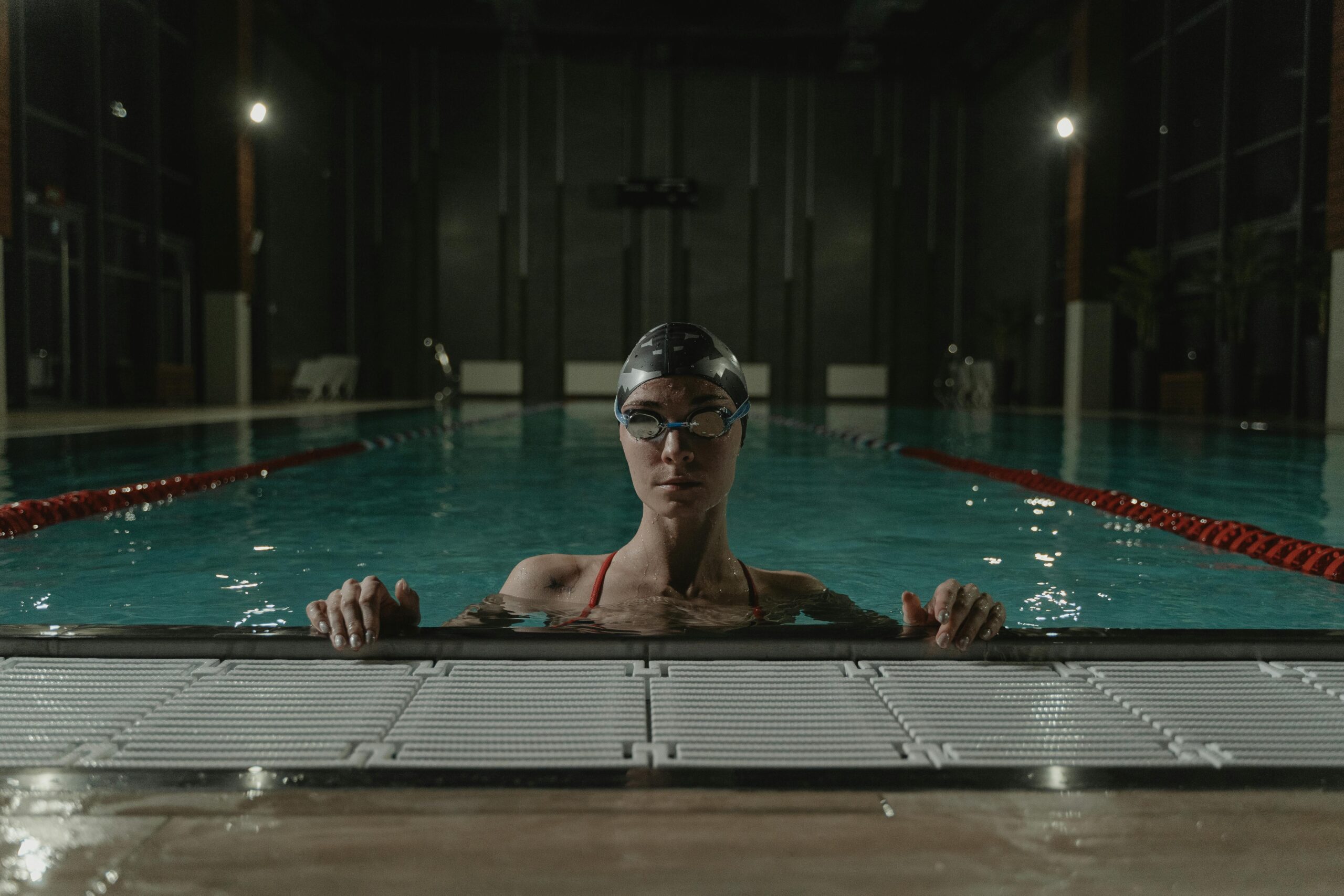 A swimmer with goggles and cap in an indoor pool, exuding determination. Nighttime setting, calm atmosphere.